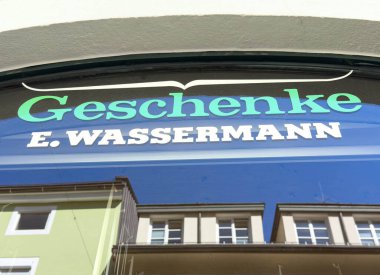 Lienz, Avusturya - 18 Eylül 2025: Hediyelik eşya dükkanı tabelası E. Wassermann 'ın çevresindeki binaların canlı renkleri ve yansımaları ile davetkar bir sahne yaratıyor.