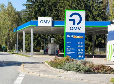 Lienz, Avusturya - 18 Eylül 2025: OMV yakıt istasyonu, ağaçlar ve parlak gökyüzü ile doğal bir manzarada dizel ve süper için görünür fiyatlar sunuyor