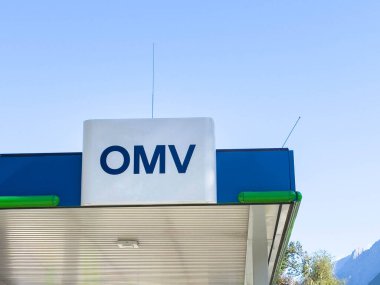Lienz, Avusturya - 18 Eylül 2025: OMV benzin istasyonu işareti belirgin bir şekilde açık mavi gökyüzüne karşı sergileniyor, marka varlığı ve mimari tasarımı vurgulanıyor