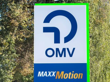Lienz, Avusturya - 18 Eylül 2025: OMV işareti ile MAXXMotion markası canlı yeşil ağaçlara karşı, yakıt hizmetleri ve enerji çözümleri vurgulandı