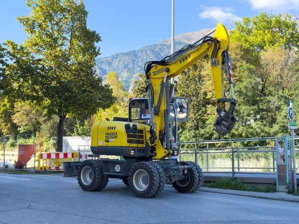 Lienz, Avusturya - 18 Eylül 2025: Sarı kazıcı caddeye park edilmiş, sağlam yapısını ve mekanik özelliklerini güzel doğal arkaplan arasında vurguluyor