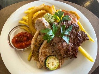 Kızarmış et tabağı, yanında patates kızartması ve soğan halkası..