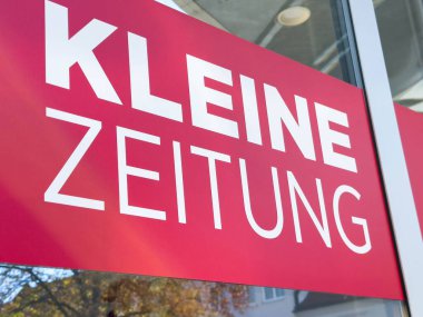 Wolfsberg, Avusturya - 19 Eylül 2025: Parlak kırmızı vitrin levhası Kleine Zeitung 'u gösteriyor, açık görüş mesafesi olan bir şehir ortamında yerel bir gazeteyi gösteriyor