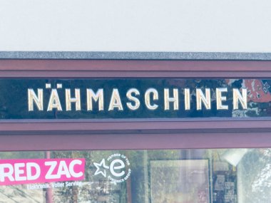 Wolfsberg, Avusturya - 19 Eylül 2025: Nahmaschinen, renkli mağazalar ve reklamlarla çevrili kentsel alanda dikiş makinesi atölyesini ön plana çıkarıyor