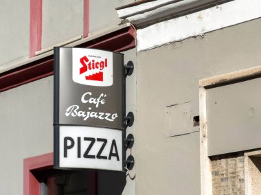 Wolfsberg, Avusturya - 19 Eylül 2025: Stiegl Cafe Bajazzo pizza tabelası dış bina üzerinde parlak renkler ve yemek atmosferi için davetiye tasarımı