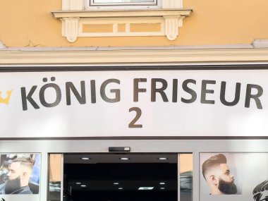 Wolfsberg, Avusturya - 19 Eylül 2025: Konig Friseur berber dükkanı modern tasarım ve stil tabelaları sunarak kentsel bir çevrede saç kesimi ve bakım hizmetleri sunmaktadır.