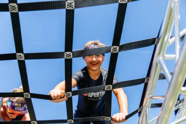 Villach, Avusturya - 20 Eylül 2025: Genç çocuk arkasında parlak mavi bir gökyüzü olan Sparta yarış engelinde hevesle yol alıyor