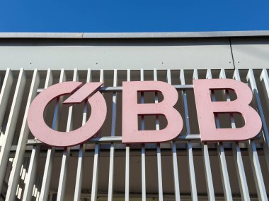 Bleiburg, Avusturya - 19 Eylül 2025: OBB logosu, dikey levhalar ve parlak mavi gökyüzü ile modern bir ambiyans oluşturulmasında kullanılmıştır.