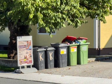 Bleiburg, Avusturya - 19 Eylül 2025: Çöp bidonları, yeşillik ve yerel hizmetler için bir tanıtım işareti ile sokakta düzgünce düzenlenir