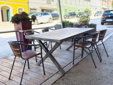 Bleiburg, Avusturya - 19 Eylül 2025: Çiçekler ve renkli binalarla çevrili ahşap sandalyeli modern açık hava yemek masası