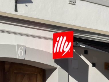 Bleiburg, Avusturya - 19 Eylül 2025: Illy cafe tabelası bir binanın ön cephesinde beyaz arka planda çarpıcı kırmızı bir logo ile gösterildi