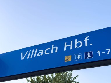 Villach, Avusturya - 19 Eylül 2025: Villach Hbf tabelası Avusturya 'da önemli bir ulaşım merkezini temsil eden açık mavi gökyüzü üzerinde belirgin bir şekilde sergilendi
