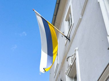 Açık gökyüzüne karşı dikey mavi, sarı ve beyaz bayrak.