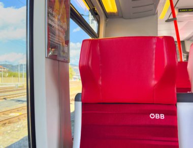 Sankt Veit Ad Glan, Avusturya - 17 Eylül 2025: OBB treninde kırmızı tren koltuğu, çağdaş tasarımı ve pencerenin dışındaki güzel manzarayı vurguluyor