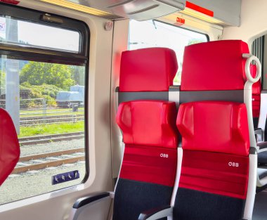 Sankt Veit Ad Glan, Avusturya - 17 Eylül 2025: Kırmızı koltuklu ve geniş pencereli modern bir trenin iç mekanı, dış manzaraya bir bakış sağlıyor