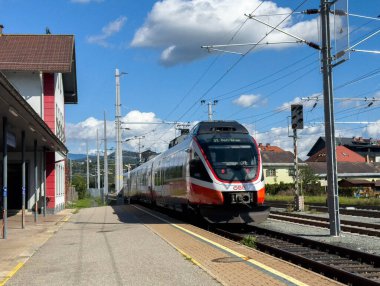 Sankt Veit Ad Glan, Avusturya - 17 Eylül 2025: Elektrik treni hareketli bir çevre ve açık gökyüzü ile birlikte manzaralı istasyona yaklaşıyor, seyahat deneyimini vurguluyor