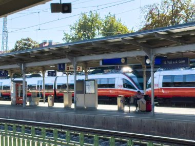 Sankt Veit Ad Glan, Avusturya - 17 Eylül 2025: Tren istasyonu platformunda modern trenler, açık tabela ve yolcu oturma ortamı vurgulanıyor