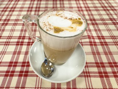 Cam bardakta köpüklü latte ve kareli masa örtüsünde tarçın..