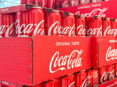 Gemona, İtalya - 24 Eylül 2025: Parlak kırmızı kutularda istiflenmiş Coca-Cola kutuları orijinal tadı vurguluyor, perakende ortamında çarpıcı bir görsel görüntü yaratıyor