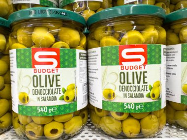 Gemona, İtalya - 24 Eylül 2025: S bütçeli kavanozlarda bulunan yeşil zeytinler süpermarket raflarında, mutfak yemekleri ve sağlıklı atıştırmalıklar için ideal bir şekilde düzenlenmiştir.