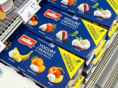 Gemona, İtalya - 24 Eylül 2025: Müller yoğurt kutuları bir süpermarkette dizilmiş, muzlu, şeftalili ve parlak ambalajlı vişne gibi tatları vurguluyor