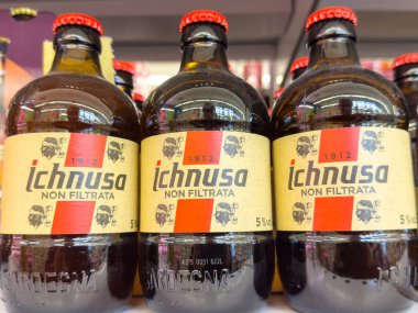 Gemona, İtalya - 24 Eylül 2025: Bir rafta sergilenen Ichnusa Non Filtrata bira şişeleri, renkli etiketler ve kehribar sıvısıyla eşsiz Sardunya markasını vurguluyor