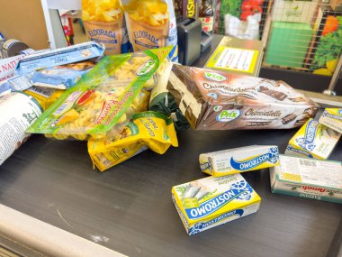 Gemona, İtalya - 24 Eylül 2025: Bakkal kasası makarna, çikolata ve tereyağı gibi çeşitli gıda ürünlerini sergiliyor, alışverişin özünü yakalıyor