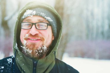 Mutlu genç sakallı adam gün batımında kış ormandaki soğuk havalarda closeup portresi. Eğlenceli adam gülümsüyor. Yüz, sakal, bıyık ve buğulu, gözlük frost ile kaplı.