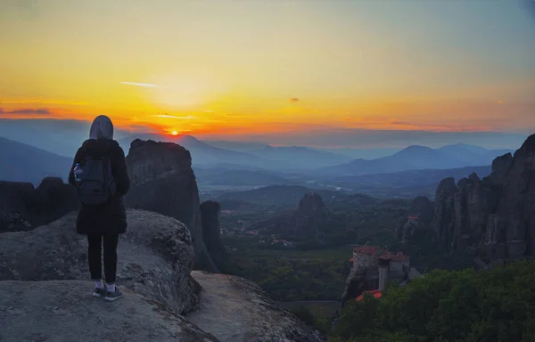 Happy woman stay on the peak of the mountain cliff edge under sunset light sky enjoying the success, freedom and bright future. Monastery Meteora Kalambaka in Greece on background.