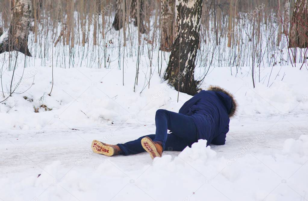Young people in stylish clothes slipped on a slippery road during a walk on a birch grove. The guy fell and trying to stand up.