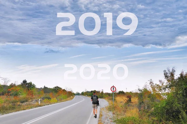 Man traveler walking alone along road to goals 2020 2021 new year. Danger to 2019 year concept with rainstorm clouds. Success, passing time, future concept Empty asphalt road Leaving behind old years