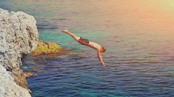 Fiatal férfi jumping off Cliff a Blue Water Ocean naplementekor. Törvény — Stock Fotó