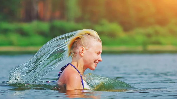 Active young blonde woman splashing water in river. Beautiful he