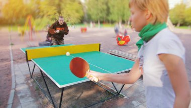 Grup mutlu genç arkadaşlar, kız ve çocuk, açık havada topu ile ping pong masa tenisi oynuyor. Sağlıklı spor ve hakiki duygular kavramı. Aktif yaşam tarzı, eğlenceli dinlenme. İki kişi veya oyuncu oyunu.