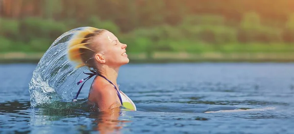 Mujer rubia joven activa agitando el pelo salpicando agua en el río. Hermosa señora sana relajarse y reír, levantando la cabeza fuera del agua. Vacaciones en el paraíso disfrutando de nadar. Congelación de movimiento . —  Fotos de Stock