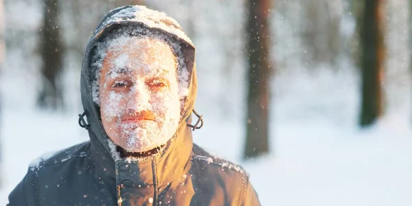 Divertido retrato de un joven congelado. Correr en una ventisca en el bosque. Rostro cubierto de nieve y escarcha. Retrato de primer plano del joven feliz sonríe en clima frío en el bosque de invierno al atardecer . — Foto de Stock