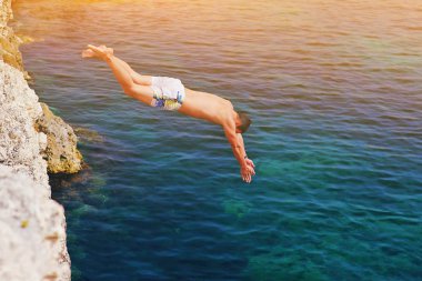 Genç adam Sunset 'te mavi su Okyanusu 'Na atlayıp Cliff 'e atlıyor. Hareket