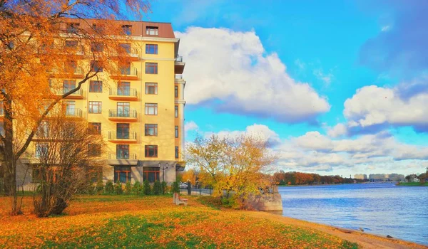 Residential building on blue river bank and bench near the autum — Stock Photo, Image