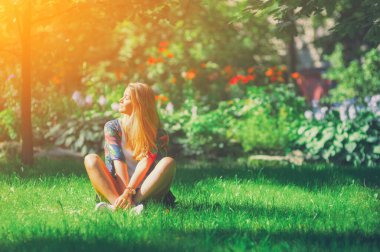 Dışarıda yoga pozisyonunda oturan mutlu özgür genç kadın yaz parkındaki çimenlerde gözleri kapalı sakin kız gülümsemenin ve bahar şehir havasında dinlenmenin tadını çıkarıyor. İç ışık konsepti. Bali asia güneş sevinci