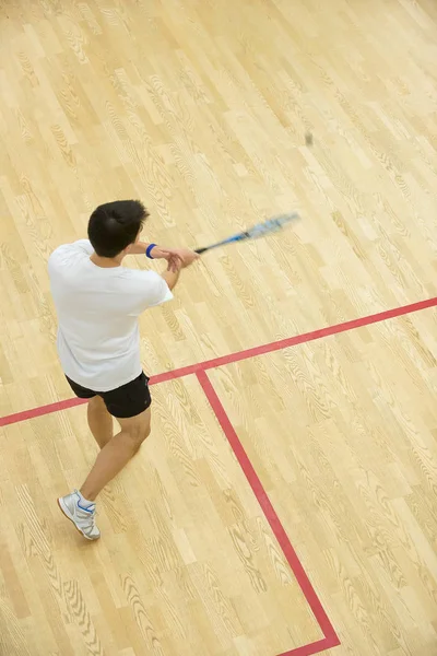 Genç adam squash oynuyor.