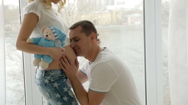 guy kisses the belly of his pregnant blonde wife standing