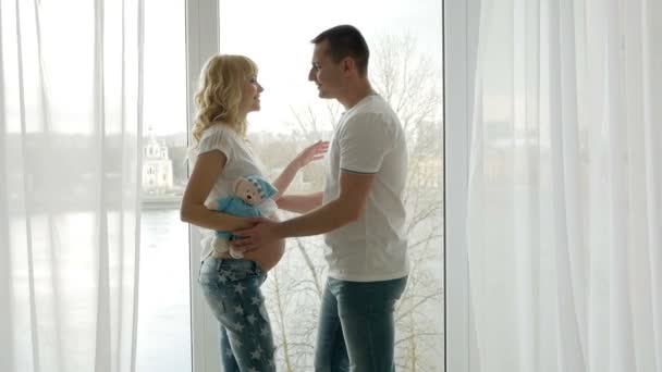 guy kisses the belly of his pregnant blonde wife standing