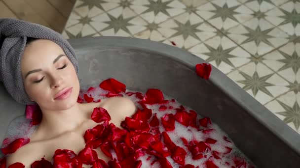 Sexy dívka spočívá ve velké kamenné lázně s růžovou květinou v ruce