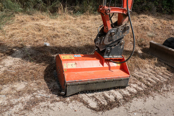 Мини-экскаватор с сочлененной рукой, очищающий края сельской дороги с помощью инструмента щеточника