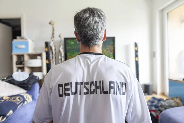 German fan sits in a Deutschland ( Germany ) jersey in front of a television