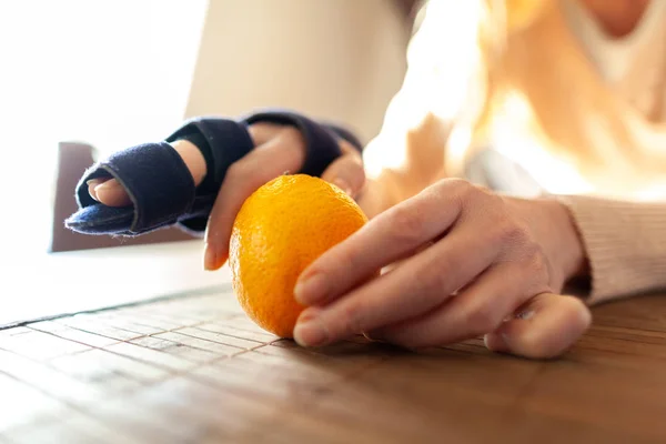 A hand peels an orange with a medical hand sling