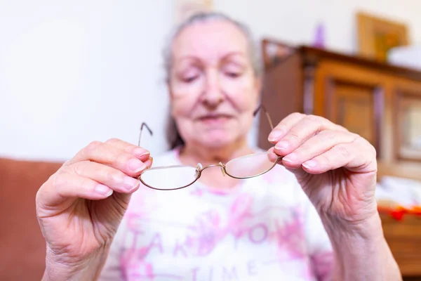 An old woman puts on her glasses