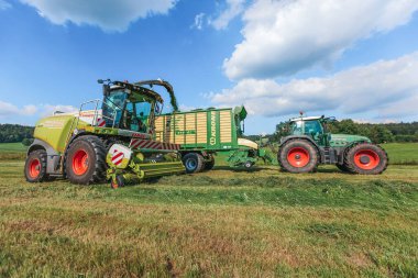 BAVARIA / GERMANY - AĞUSTOS 07.2020: Claas hasatçısı ve Krone ZX400GL karavanı olan bir Fendt 926 bir tarla üzerinde çalışıyor.