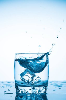 beyaz bir arka plan, bardak bardak su düşen buz parçası, her yöne uçan su sıçramalarına bir parça ile bir bardak su sıçrama