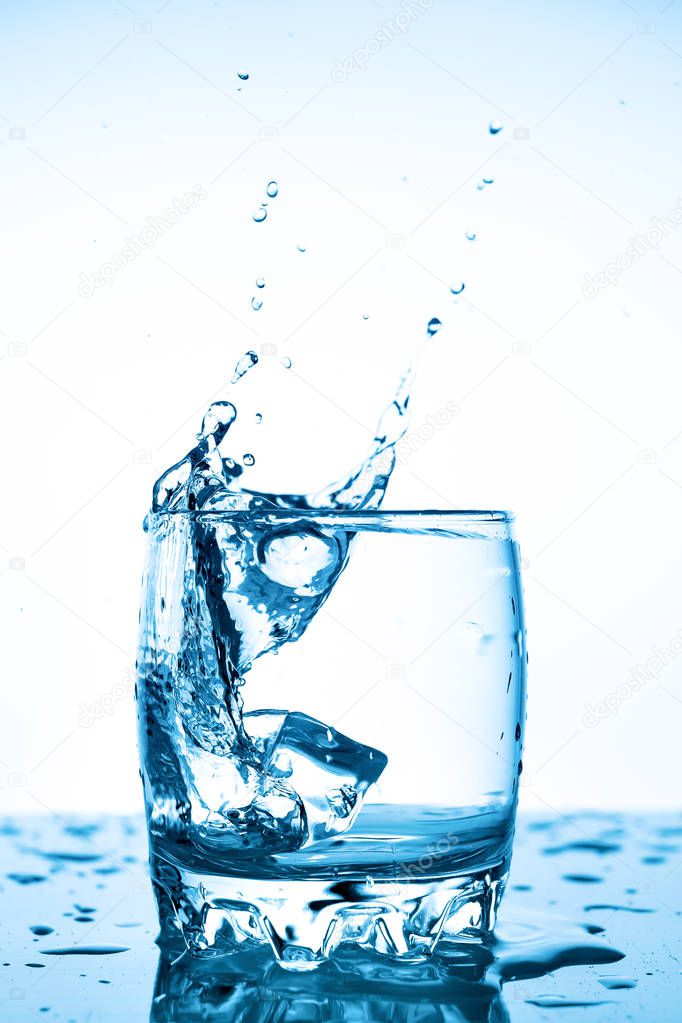 water splash in a glass with a piece of ice on a white background, a piece of ice falling into glass Cup of water, splashes of water flying in all directions